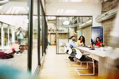 Three colleagues having a meeting in a meeting room, while one colleague is making a call outside the room.
